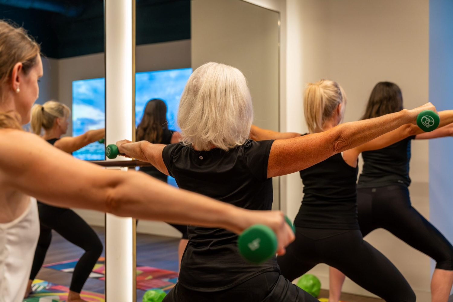 A mixed-age class working with light dumbbells in a mirrored studio