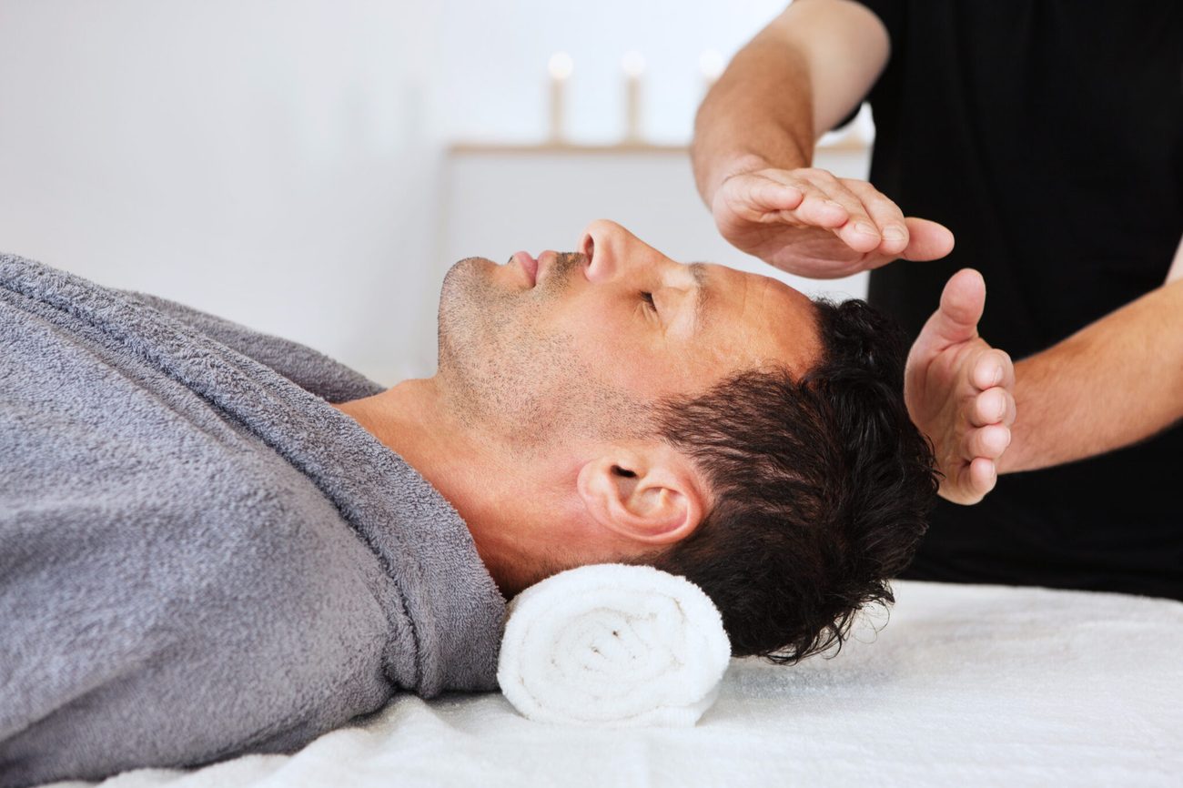 A client lying down with a practitioner's hands held above them and a singing bowl beside the couch