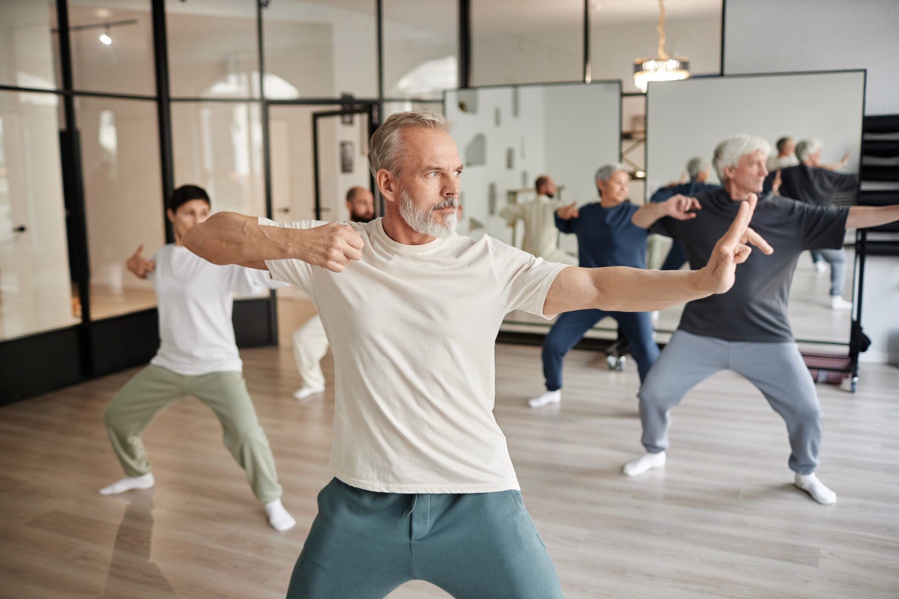 A tai chi class holding a wide stance in a mirrored studio